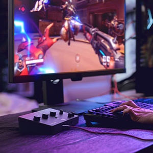 Gaming setup showing smartphone mounted on stand, displaying colorful game. Visible gaming peripherals include controller and keyboard in dimly lit environment.