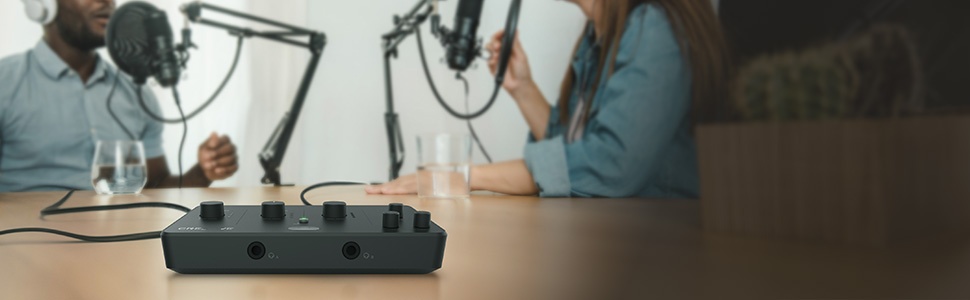 Close-up of a black multi-outlet power strip on a wooden surface. Partial view of people sitting at a table in the background.