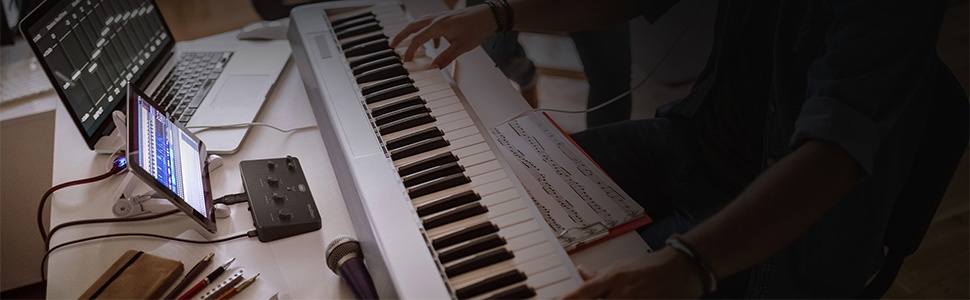 Digital piano keyboard setup with connected smartphone showing interface or app display in dim lighting conditions.