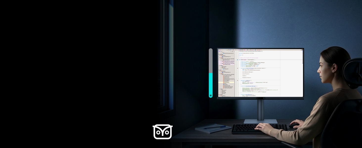 Personne assise au bureau dans une pièce sombre, face à un écran d'ordinateur éclairé affichant un document blanc ou une interface à l'écran.